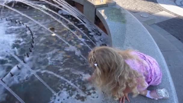 Malá blondýnka v šatech hrát s fontánou vody v létě. Ruční snímek - Záběry, video