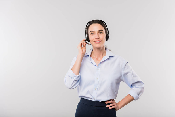 Ευτυχισμένος νέος κομψό χειριστή με ακουστικά συμβουλευτικές πελάτες σε απευθείας σύνδεση, ενώ στέκεται μπροστά από την κάμερα στην απομόνωση - Φωτογραφία, εικόνα