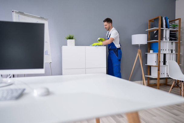 Mid Adult Male Worker Cleaning Shelf With Spray And Sponge At Office - Foto, Bild