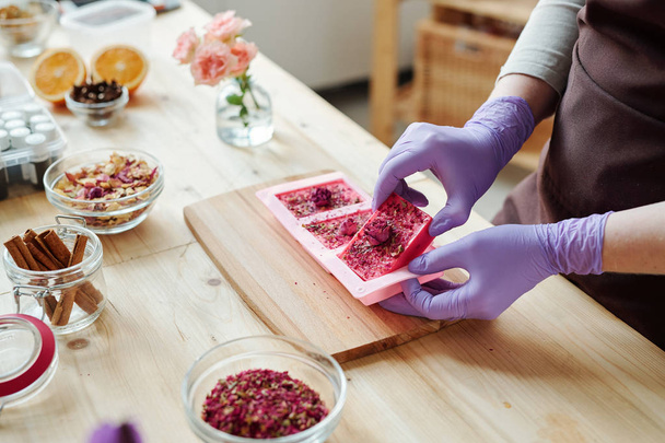 Mains de jeune femme en gants de caoutchouc lilas sortant du savon rose frais fait à la main des moules en silicone
 - Photo, image