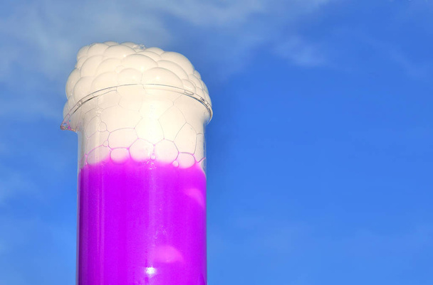 Científico sosteniendo con una solución fluorescente roja bajo la luz solar. El hielo seco produce burbujas y humo blanco
. - Foto, Imagen