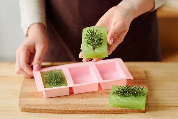 Hands of girl holding green fresh handmade soap bar with conifer on top after taking it out of silicone mold - Photo, Image