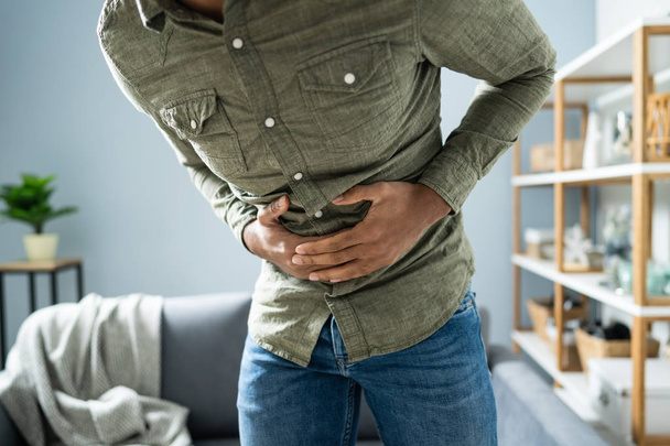Midsection Of Man With Stomach Ache Standing Near Couch At Home - Foto, immagini