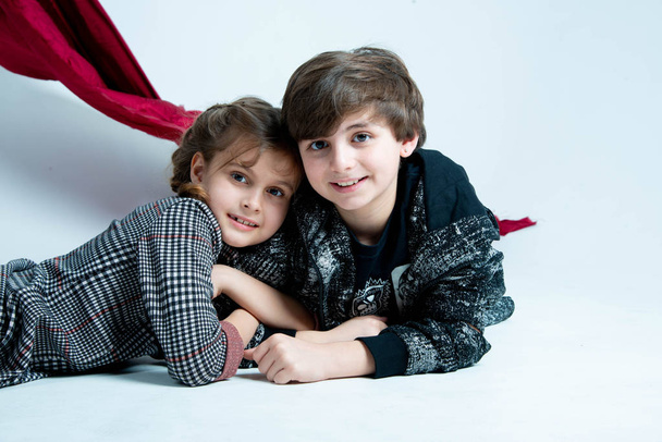 χαριτωμένα παιδιά που κάθονται στο στούντιο σε γκρι φόντο με κόκκινο καμβά - Φωτογραφία, εικόνα