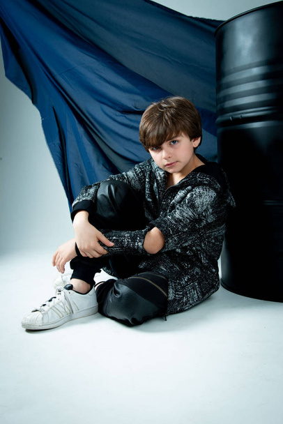 brunet kid boy sitting with black barrel on gray background - Photo, Image