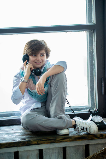 cute boy sitting on windowsill and talking by telephone - Фото, изображение