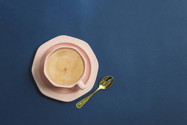 Beautiful pink cup of coffee and golden spoon on the dark blue background - Photo, Image