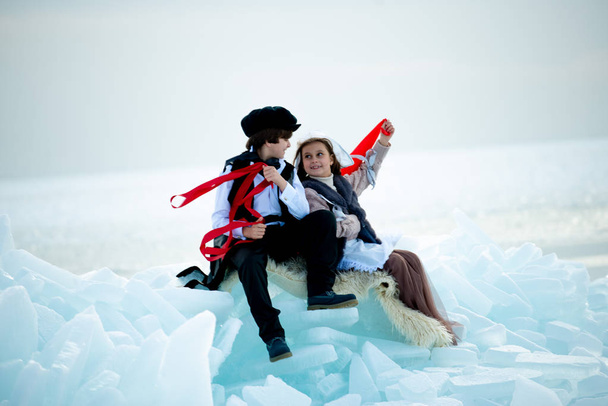 boy and girl in themed costumes with red ribbons in winter landscape - Фото, изображение