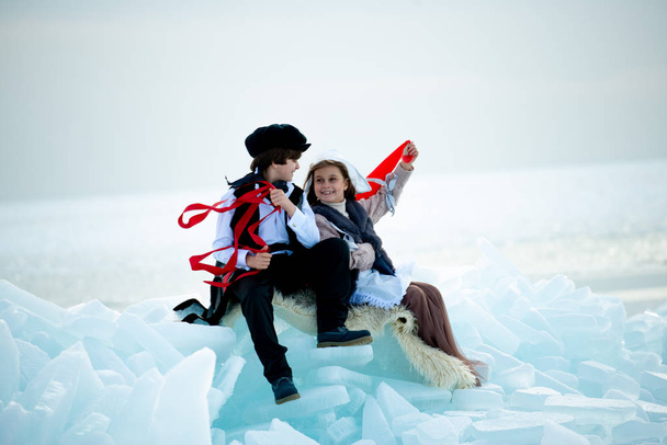 boy and girl in themed costumes with red ribbons in winter landscape - Fotoğraf, Görsel