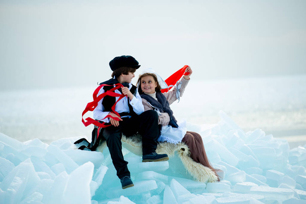 boy and girl in themed costumes with red ribbons in winter landscape - Foto, Bild