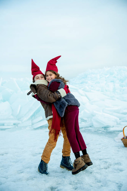 smiling children in red gnome caps hugging on ice on winter background - Foto, Imagem