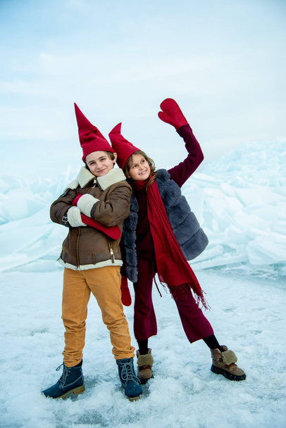 children in red gnome caps standing on ice on winter background - Photo, Image
