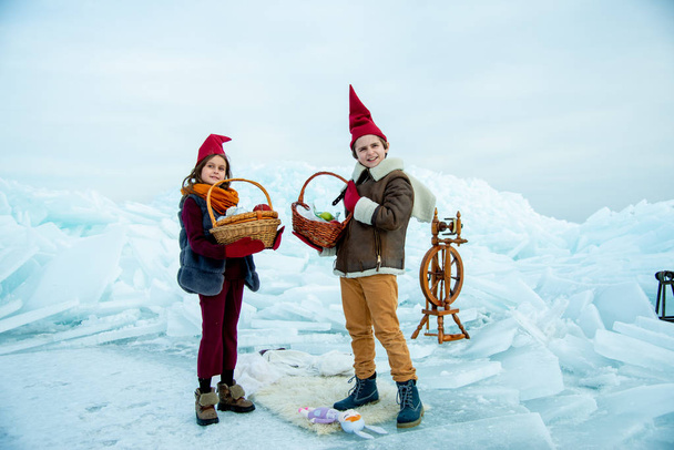 kids in red gnome caps holding picnic baskets on snow background  - Zdjęcie, obraz