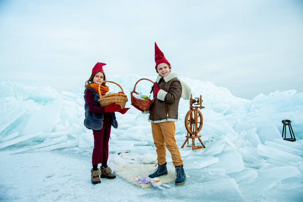 kids in red gnome caps holding picnic baskets on snow background  - Valokuva, kuva