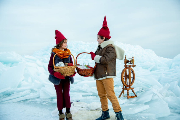 kids in red gnome caps holding picnic baskets on snow background  - Fotó, kép