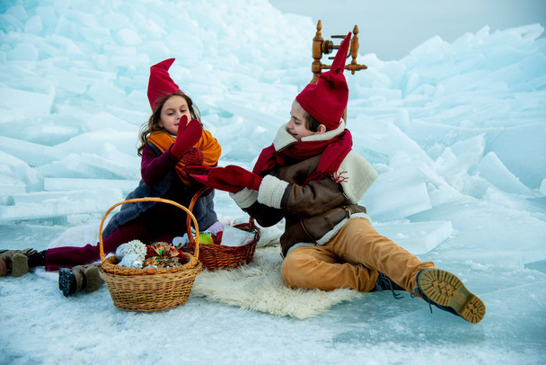 children in red gnome caps on winter picnic on snow  background  - 写真・画像
