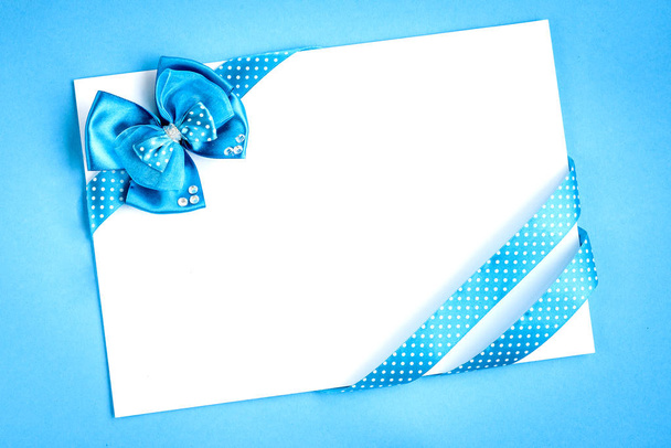 Blanco papieren notitie met blauwe linten in stippen en strik op blauwe achtergrond. - Foto, afbeelding