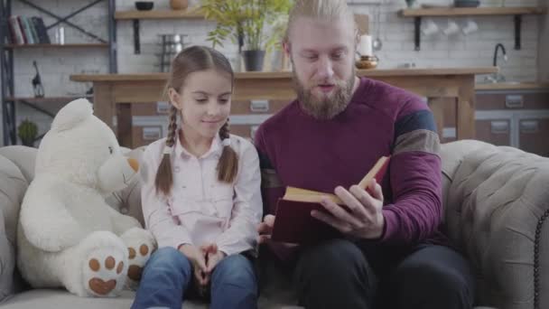 Positive Caucasian father turning page and touching daughters nose. Cute teenage girl smiling and looking at man. Adult guy educating his child at home. Fun, hobby, lifestyle. - Záběry, video
