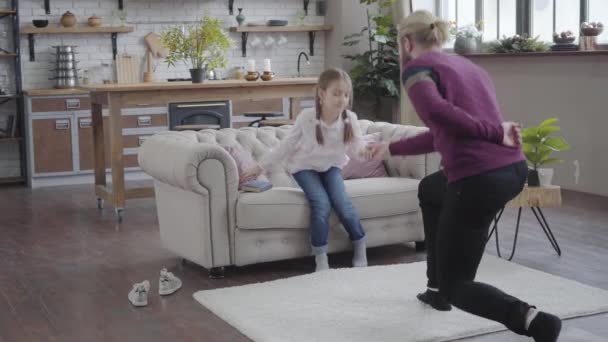 Adult Caucasian father standing on one knee and taking daughters hand. Teenage girl putting away book and dancing with father. Cheerful family spending time together. Camera approaching girl. - Metraje, vídeo
