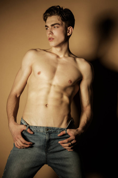 Muscle strong beautiful stripped male model in denim blue jeans on beige isolated font background - 写真・画像