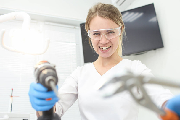 Woman dentist in white uniform holds builder instruments in hands. Selective focus - Photo, image
