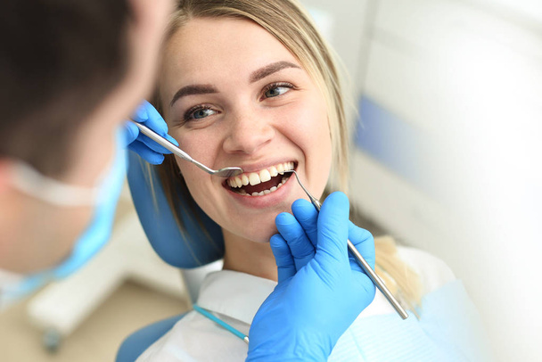 Blond female sits in dentist chair and undergo dentist checkup. Selective focus - Foto, Imagem
