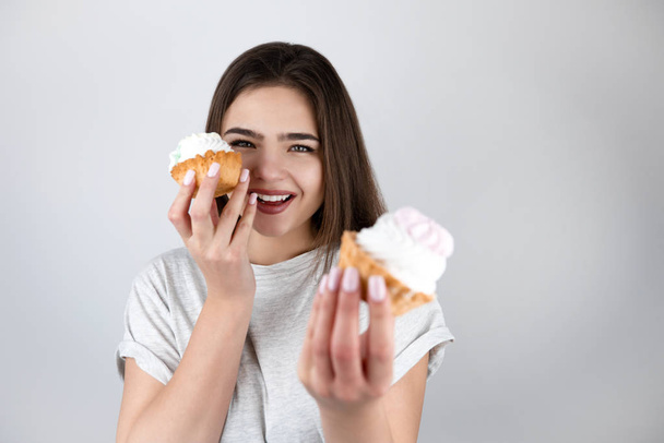 young beautiful woman holding two sweet cupcakes with cream in another looking happy isolated white background healthy lifestyle - Фото, изображение