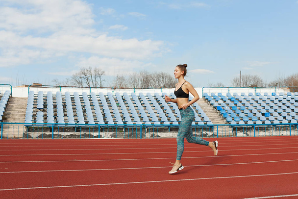 Young woman running during sunny morning on stadium track - Foto, Imagen