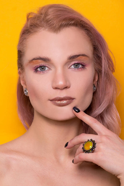 Shiny golden make-up on a beautiful young European model girl isolated on an orange background in the photo studio - 写真・画像