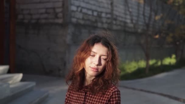 Dreaming young woman with spectacular curly red ginger hair looking at camera posing outdoor in downtown street. Female portrait. - Footage, Video