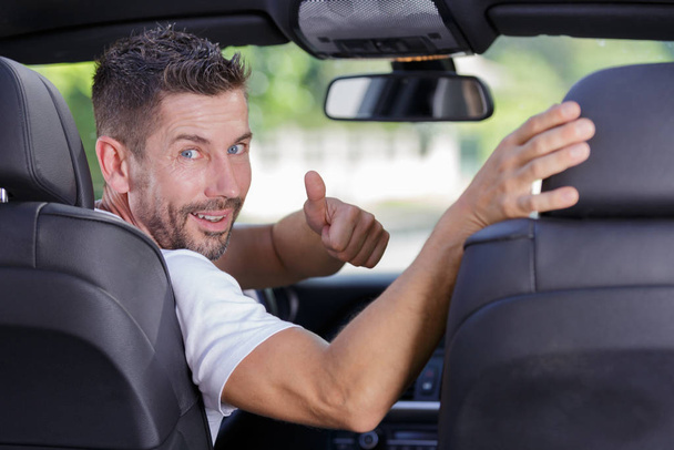 мужчина, поворачивающийся к заднему сиденью автомобиля с большими пальцами вверх
 - Фото, изображение