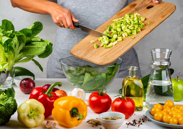 Žena přidává nakrájené avokádo do salátu ve skleněné míse, vaření v kuchyni. Zdravá strava koncepce. - Fotografie, Obrázek