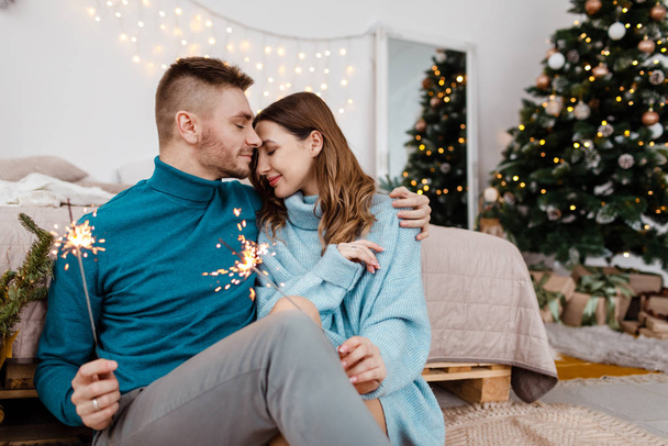 Photo of stylish loving man and pregnant woman with sparklers on background of Christmas decorations - Fotoğraf, Görsel