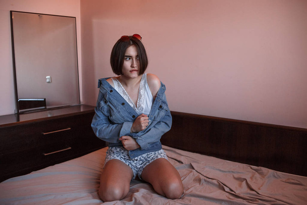 a young girl with short hair in a denim jacket and shorts sits a - Photo, Image