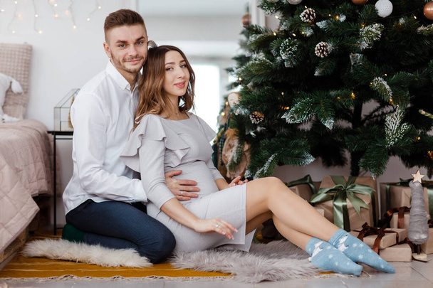 κομψό όμορφο έγκυο ζευγάρι στην αγάπη για τα Χριστούγεννα, έχοντας ένα υπόλοιπο στις διακοπές των Χριστουγέννων πριν από το νέο έτος. Μεγάλη κοιλιά έγκυος. - Φωτογραφία, εικόνα