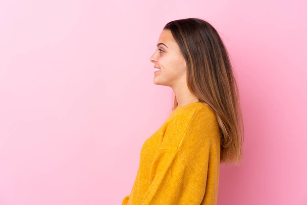 Tiener meisje met gele trui over geïsoleerde roze achtergrond in laterale positie - Foto, afbeelding
