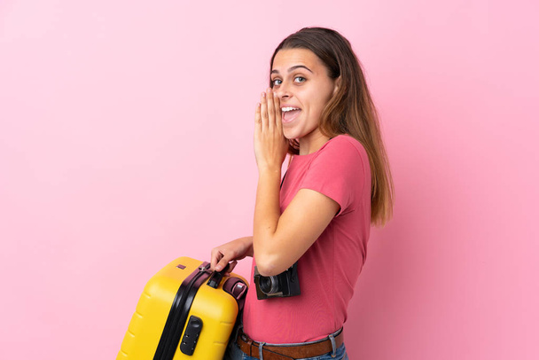 Tini utazó lány kezében egy bőrönd felett elszigetelt rózsaszín háttér suttog valamit - Fotó, kép