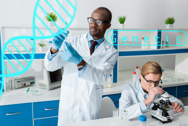 biologiste afro-américain tenant une éprouvette et se tenant près de l'illustration de l'ADN, collègue utilisant un microscope
 - Photo, image