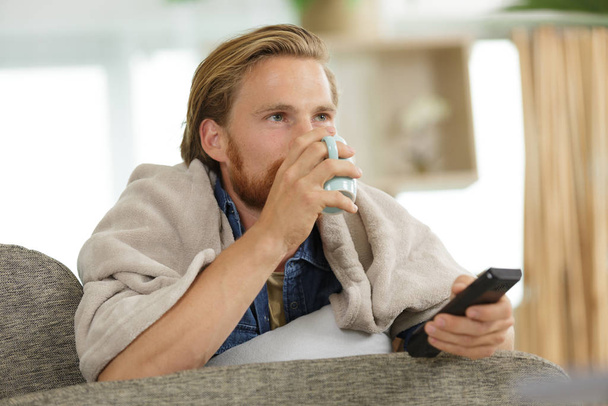young man watching tv in bed and drinking tea - Foto, afbeelding