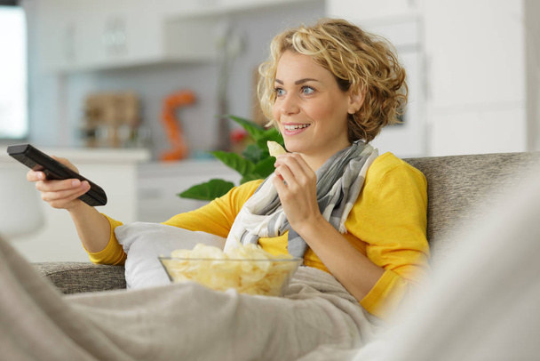 TV izlerken evde abur cubur yiyen bir kadın. - Fotoğraf, Görsel