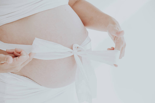 μια έγκυος γυναικεία κοιλιά και δώρο λευκό φιόγκο - Φωτογραφία, εικόνα