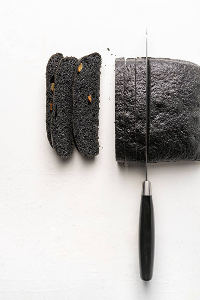 Hoja de brea de carbón parcialmente cortada, cuchillo de pan sobre fondo blanco
 - Foto, imagen