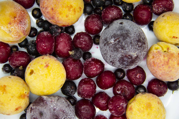 Een Berry mix van bevroren bessen, abrikozen, pruimen, kersen. Een bevroren bessen uit de vriezer. Een zoete achtergrond met diepgevroren pruim, bes, abrikoos en kers. Een gezonde bessen op de achtergrond. - Foto, afbeelding
