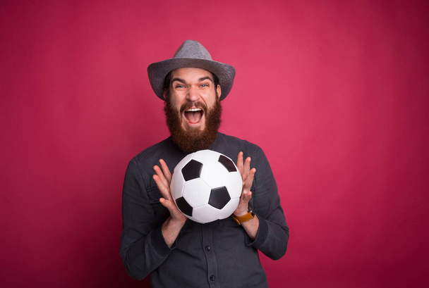 Amazed bearded man holding soccer ball and screaming - Фото, изображение