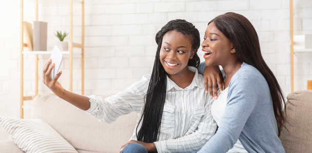 Two joyful afro girlfriends taking selfie, spending time together at home - Foto, afbeelding