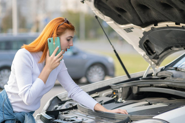 Young woman standing near broken car with popped hood talking on - Foto, Bild