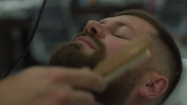 Close up of barbers hand cleaning mans beard with wooden brush in slow motion.  - Filmmaterial, Video