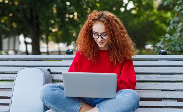 Smart female student using laptop in park - 写真・画像