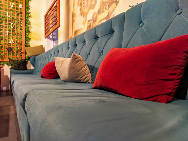 Зручний розкладний диван синього кольору з червоними подушками та орнаментами навколо, затишний і гарний дизайн інтер'єру
. - Фото, зображення