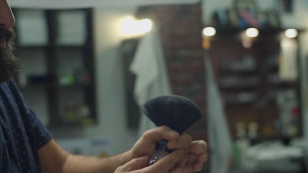 Barber hand applying talc on mans face with beard by barbers brush in slow motion.  - Metraje, vídeo